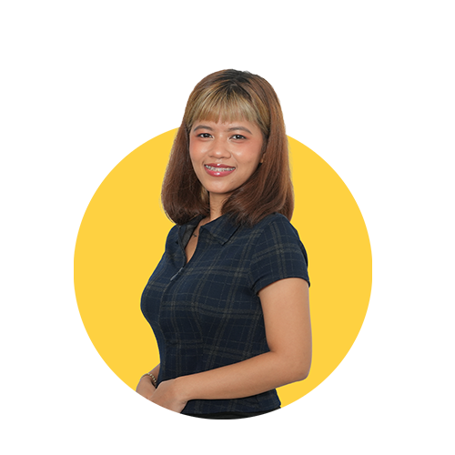 A smiling woman with shoulder-length light brown hair wearing a dark plaid shirt stands against a yellow background.