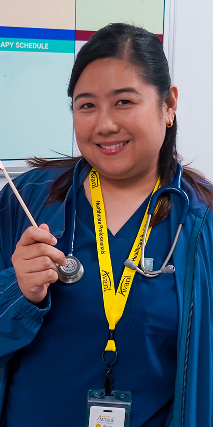 A smiling healthcare professional wearing a blue uniform, stethoscope, and yellow lanyard with "Avani" and "Healthcare