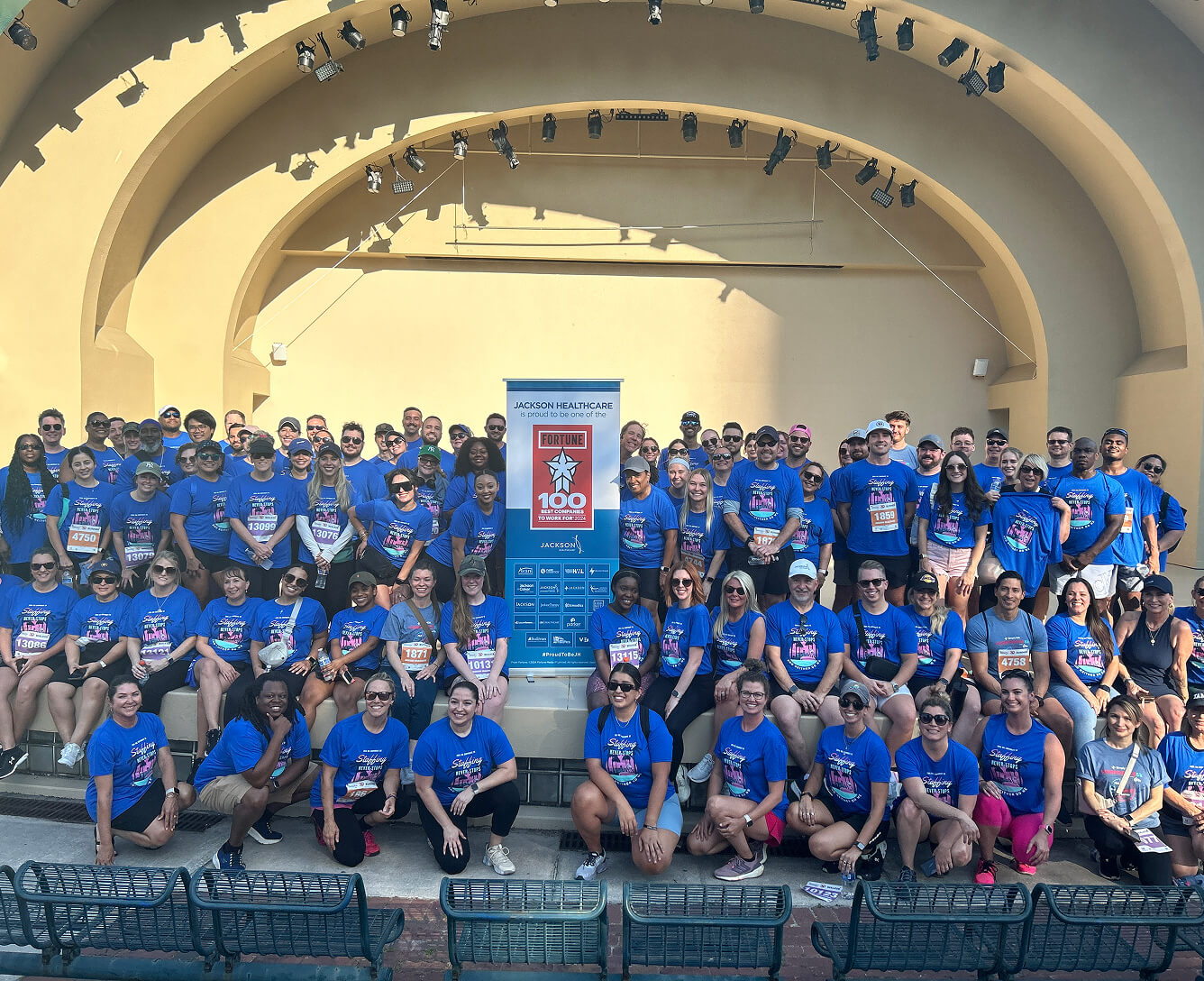 Group of diverse people wearing matching blue shirts at a charity event under a yellow arch.