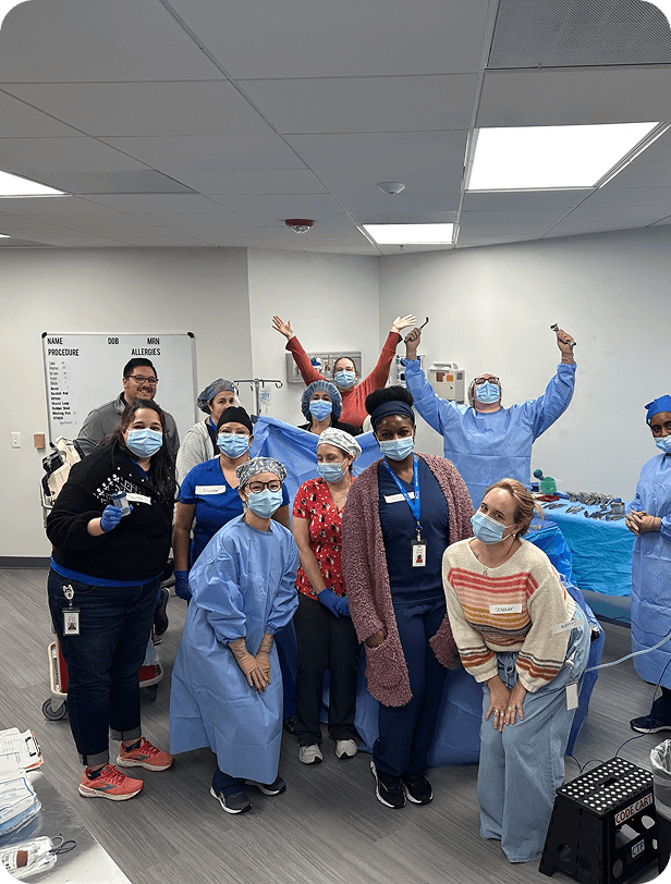Group of healthcare professionals and staff in scrubs and masks celebrating in a hospital room.
