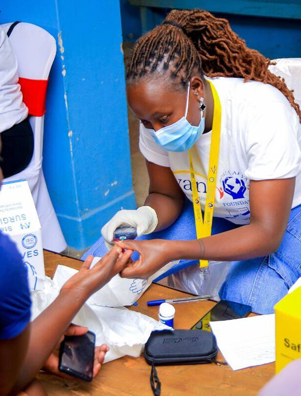 A woman in a face mask and gloves performs a medical procedure on a person's finger during a health outreach event.