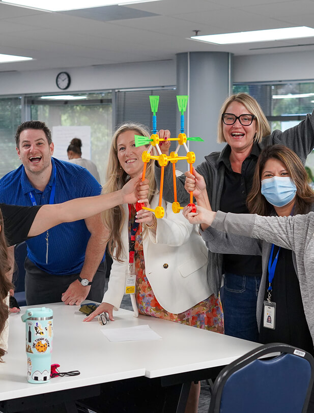 Group of diverse colleagues celebrating and holding a colorful, interconnected toy structure in an office setting.
