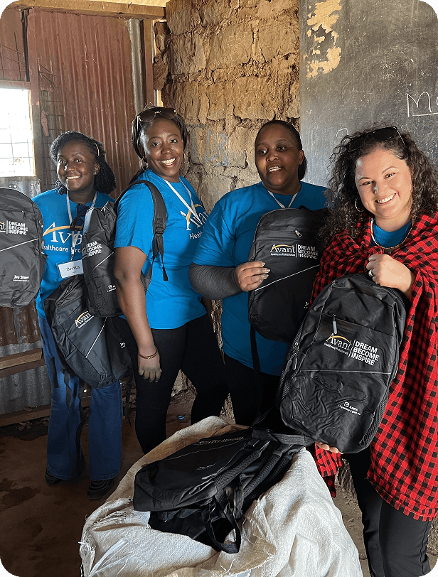 Four women in blue "Avant" t-shirts with backpacks stand inside a rustic building, smiling and holding their backpacks.