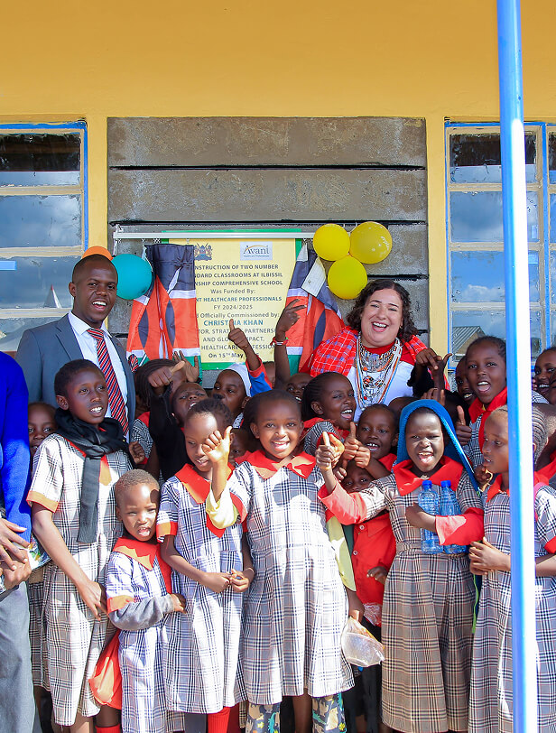 Children and two adults celebrating the opening of a new classroom, with balloons and a sign in the background.