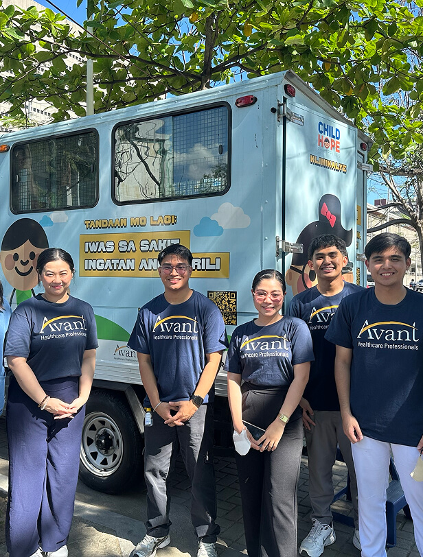 Five healthcare professionals stand in front of a mobile health unit with a cheerful message about health and hope.