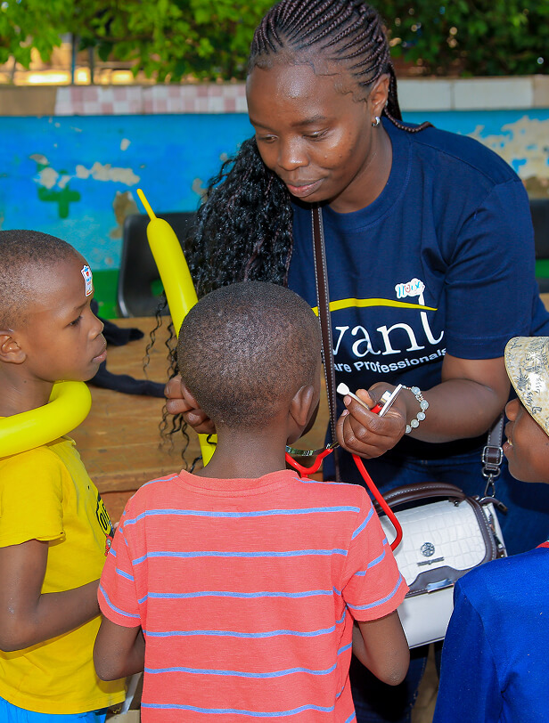A woman with braided hair uses a stethoscope to examine two children outdoors, with a colorful wall and greenery in the