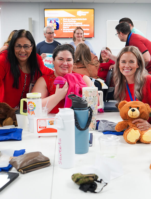 Group of diverse women smiling and celebrating with stuffed animals and gifts at a conference table.