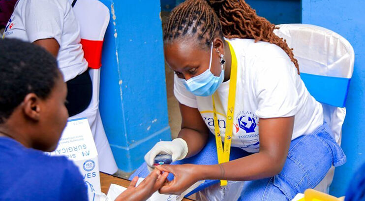 A healthcare worker in a mask and gloves checks a patient's finger during a medical outreach event.