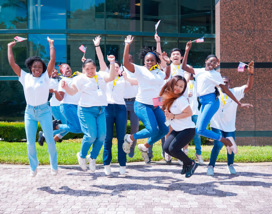 Group of diverse young women celebrating outside, holding American flags, and jumping with excitement.