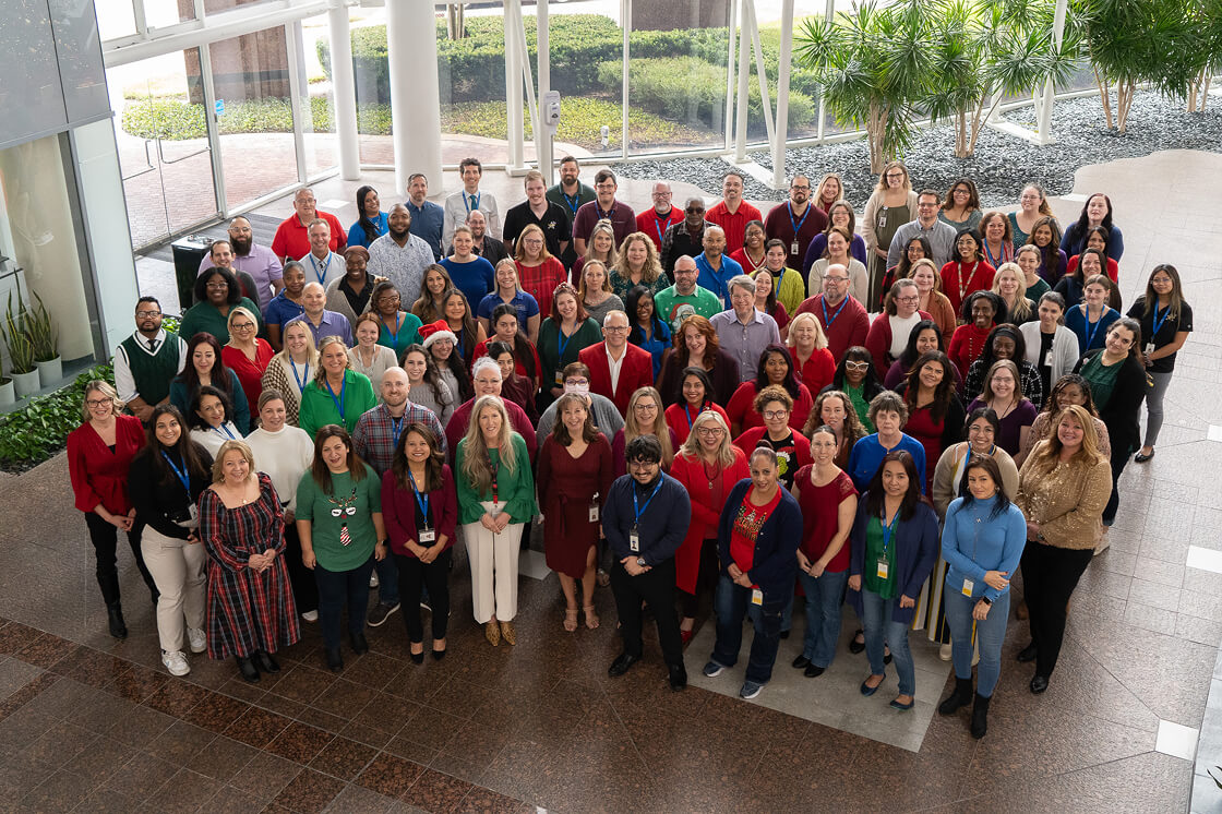 A large diverse group of people gathered indoors for a group photo, many wearing colorful clothing and conference badges.