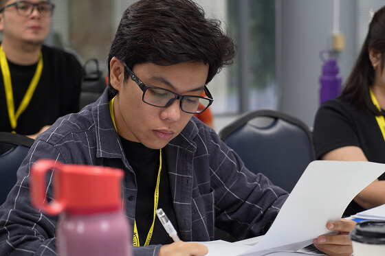 A young man with glasses and a plaid shirt reviews documents at a conference table during the Avant-International-Candidates-