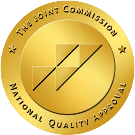 A gold circular logo with "The Joint Commission" and "National Quality Approval" around the edge, featuring a stylized