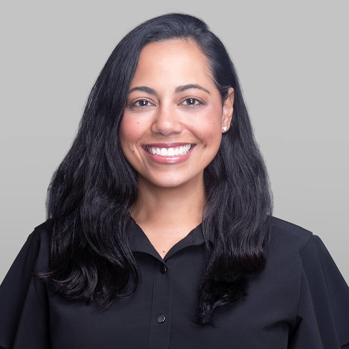 Cynthia Martinez-Patin with long black hair, smiling, wearing a black shirt against a light gray background.