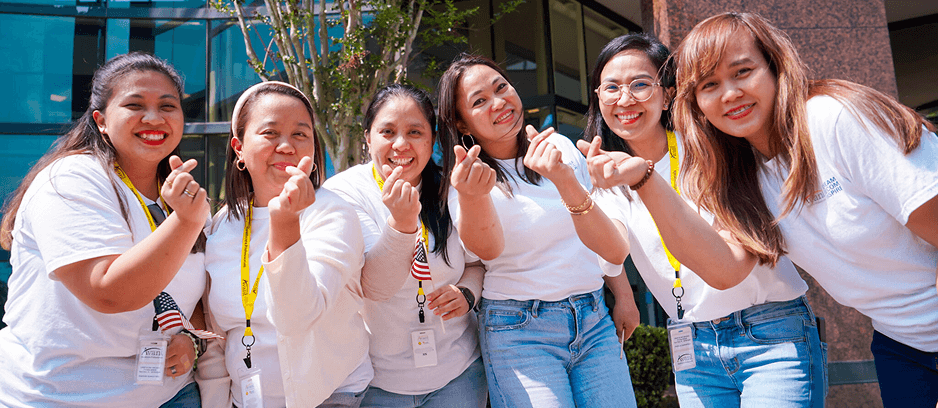 Group of diverse nurses smiling and making heart gestures outdoors in front of a modern building.