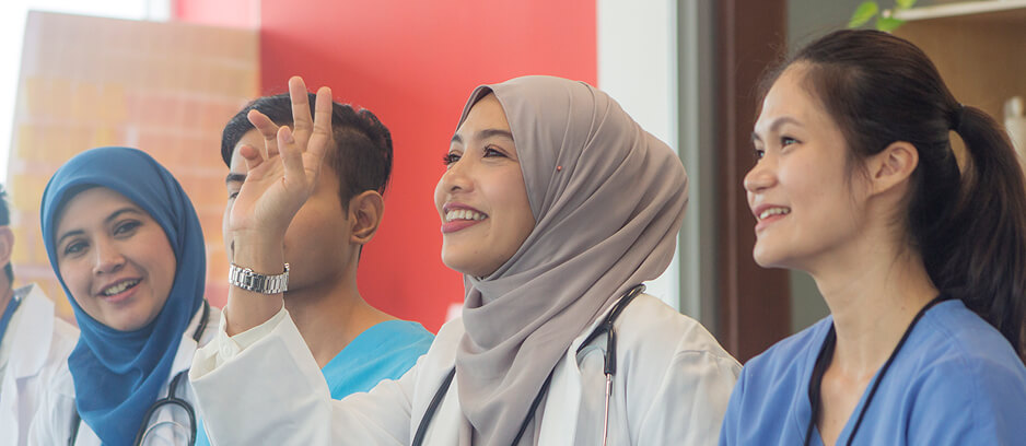 A diverse group of healthcare professionals, including women in hijabs and scrubs, smiling during a training session.
