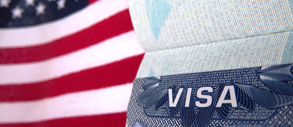 A close-up of a U.S. visa document with a blurred American flag in the background.