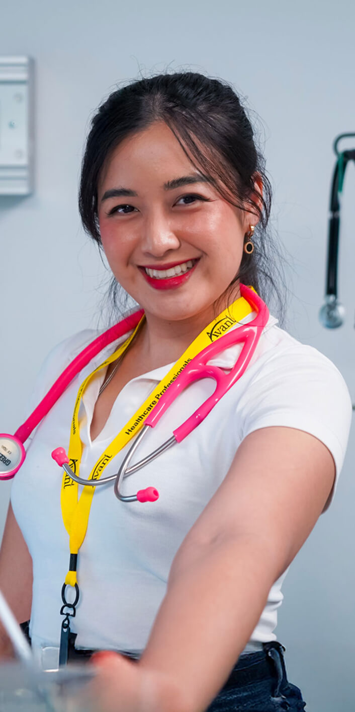 A smiling female healthcare professional with a pink stethoscope around her neck, wearing a white uniform and a yellow
