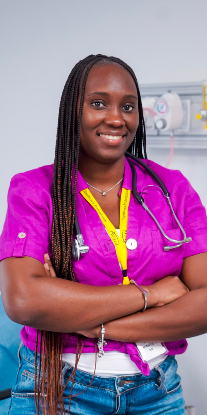 A smiling healthcare professional with braided hair, wearing a pink scrub top, stethoscope, and yellow lanyard, standing