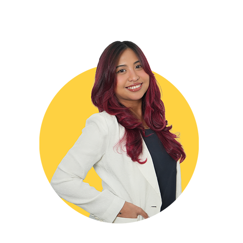 A smiling woman with long, wavy red hair wearing a white blazer and dark top stands against a yellow background.