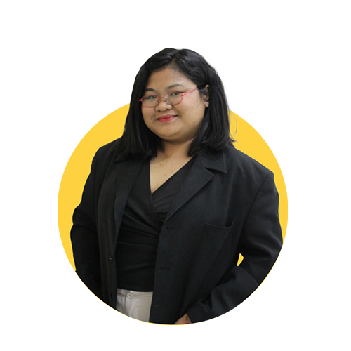 A woman with shoulder-length black hair, glasses, and a black blazer smiles confidently against a yellow background.