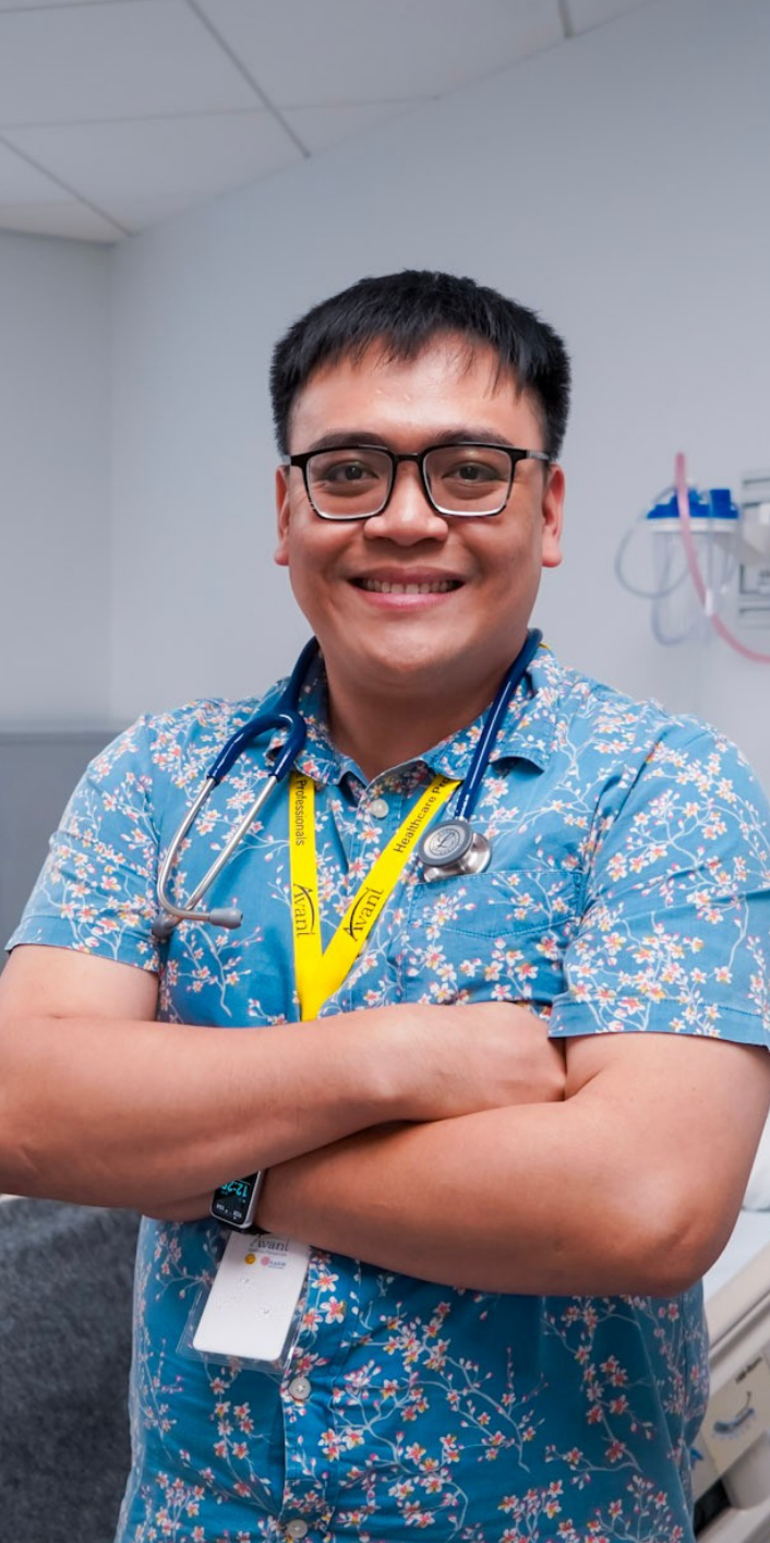 A smiling healthcare professional with glasses, wearing a floral shirt and stethoscope, standing confidently in a medical