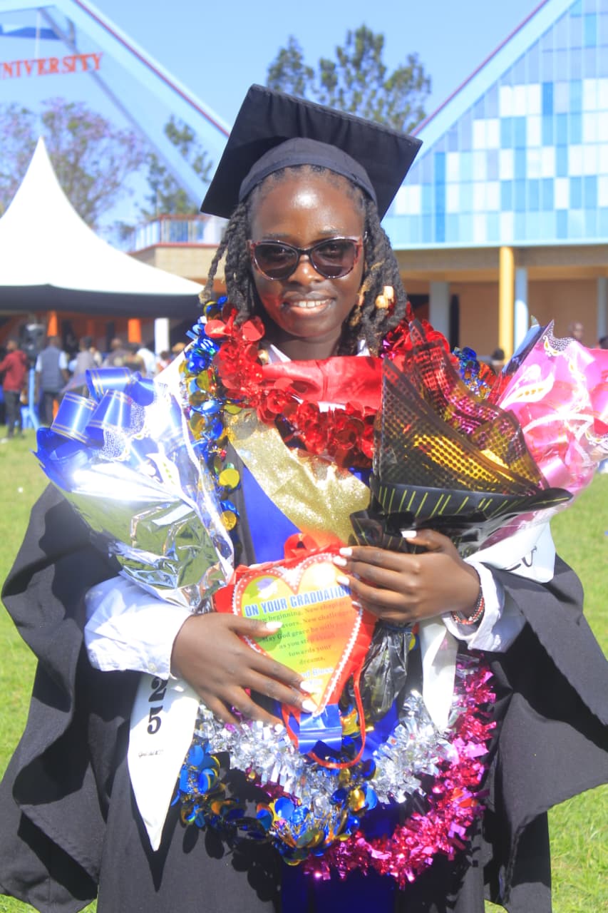 Milcah in graduation attire holding a bouquet and a heart-shaped card, celebrating her graduation outdoors.