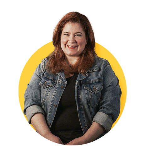Pat, a woman with shoulder-length red hair, is smiling and wearing a denim jacket against a yellow background.