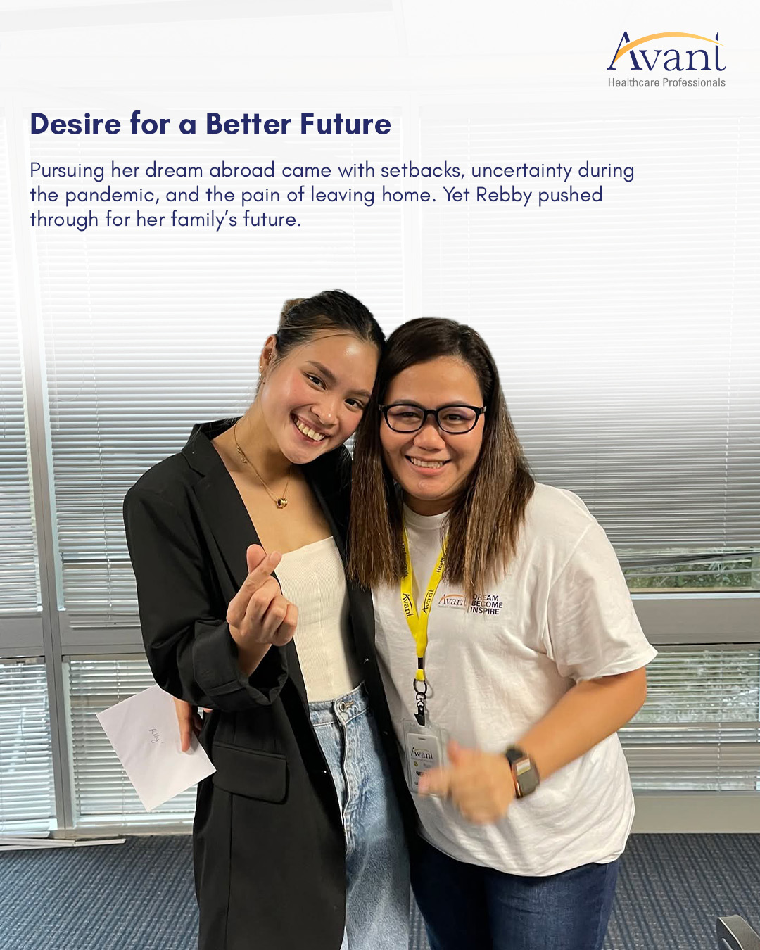Two women smiling and posing together indoors, one making a finger heart gesture, with blinds and a logo in the background.