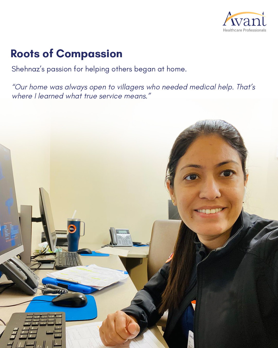 Shehnaz, smiling, sits at a desk with multiple monitors, a keyboard, and papers, wearing a black jacket in an office setting.