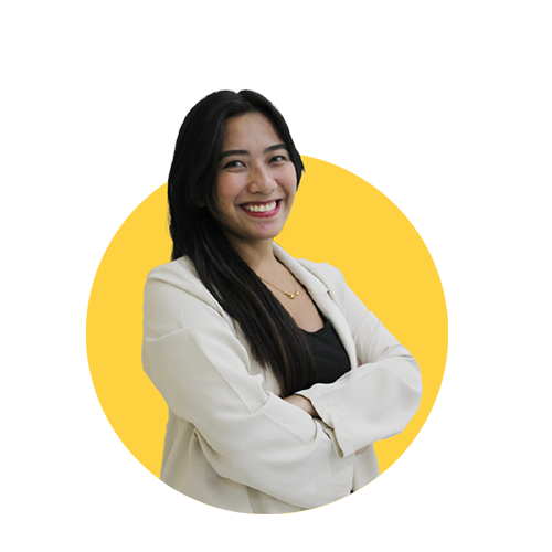 A smiling woman with long dark hair, wearing a white blazer over a black top, stands confidently with arms crossed against a