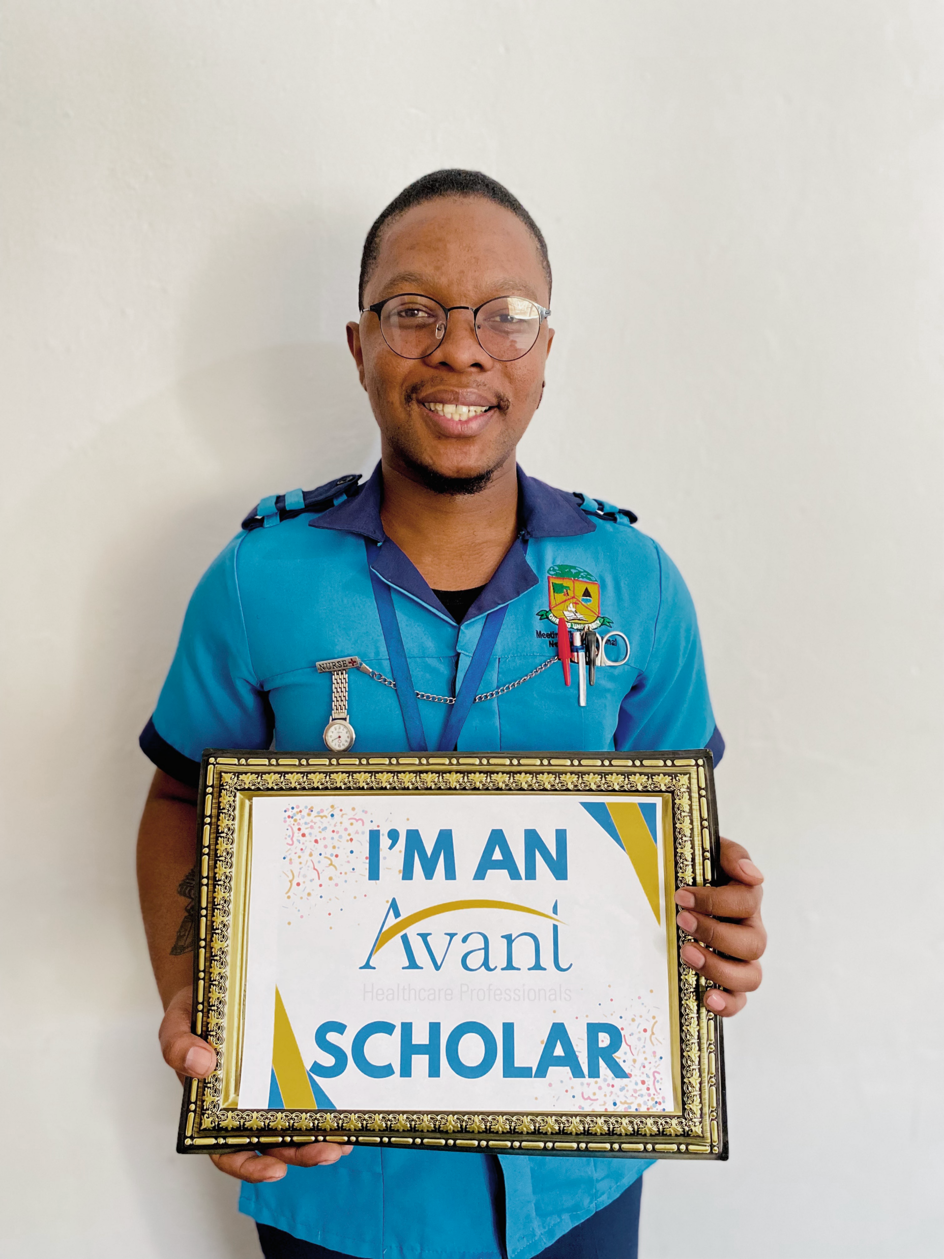 A smiling man in a blue uniform holding a framed scholarship certificate that reads "I'M AN Ivani SCHOLAR."