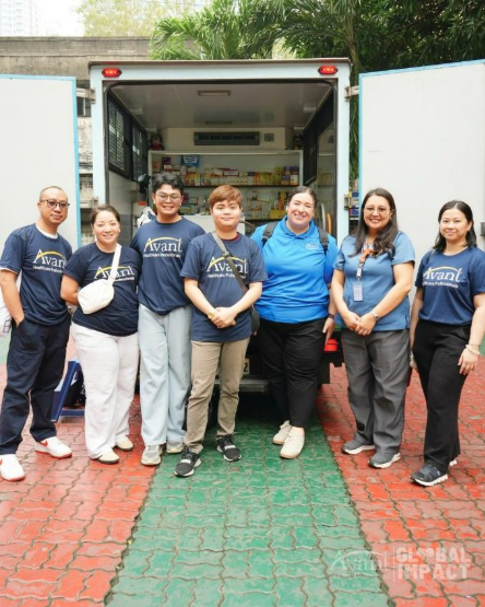 Six volunteers stand in front of a mobile food truck, smiling and wearing matching "Avani" shirts.