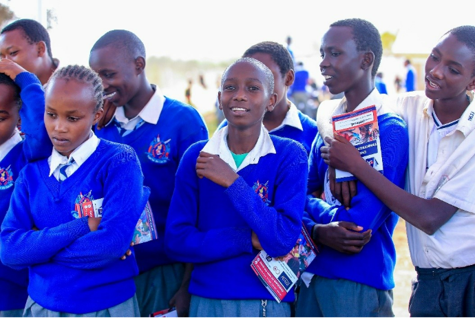 Group of students in blue uniforms smiling and interacting outdoors during daytime.