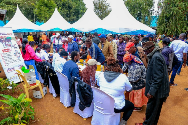 A large group of people gather under white tents at an outdoor event, engaging in conversations and activities on a sunny