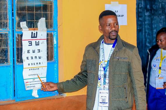 A man points at an eye chart on a window during an eye check-up event.