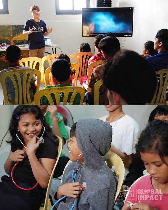 Children in a classroom listening to a teacher and engaging with stethoscopes, smiling and interacting happily.